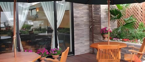 Un espace extérieur aménagé en terrasse, avec des meubles en bois, notamment des tables et des chaises, et un grand parasol pour créer de l’ombre.