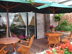 An outdoor patio area with wooden furniture, including tables and chairs, and a large umbrella providing shade. - Hotel WBF Abiyanpana Ishigakijima (Ishigaki)