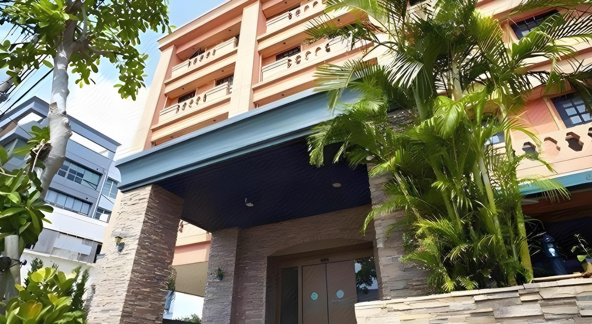 A multi-story hotel with a covered entrance, stone pillars, and a balcony with plants.