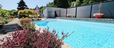Una piscina con borde de piedra, rodeada de plantas en macetas y una terraza de madera.
