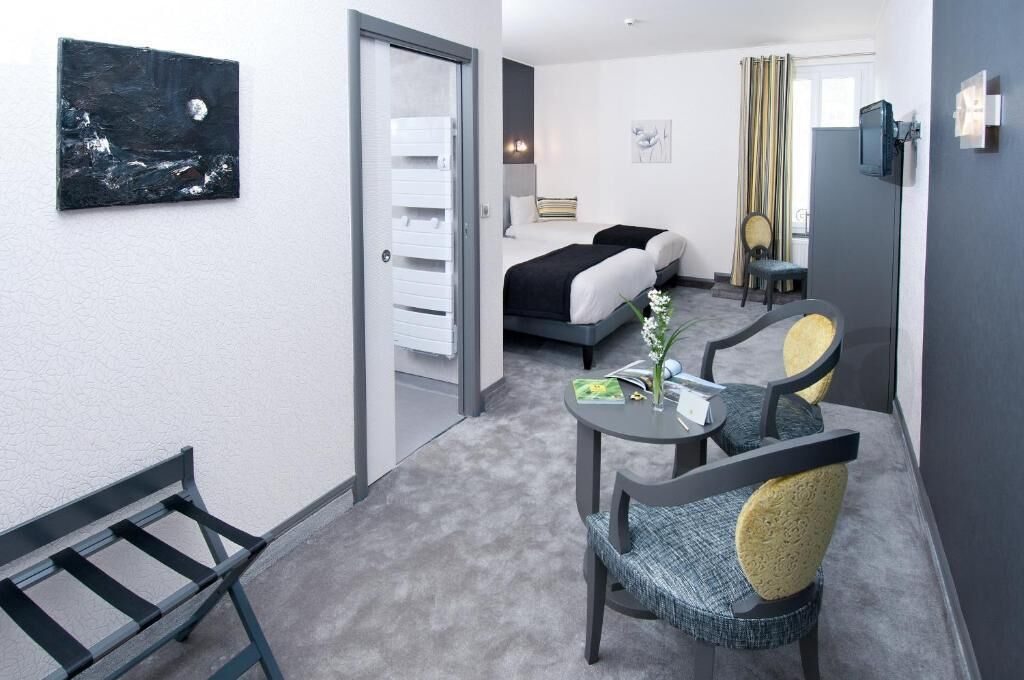 Una habitación de hotel con cama, mesitas de noche, un escritorio con sillas, un cuadro en la pared y una ventana con cortinas.