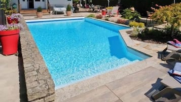 A rectangular swimming pool with a stone border, surrounded by a patio area with lounge chairs and umbrellas.