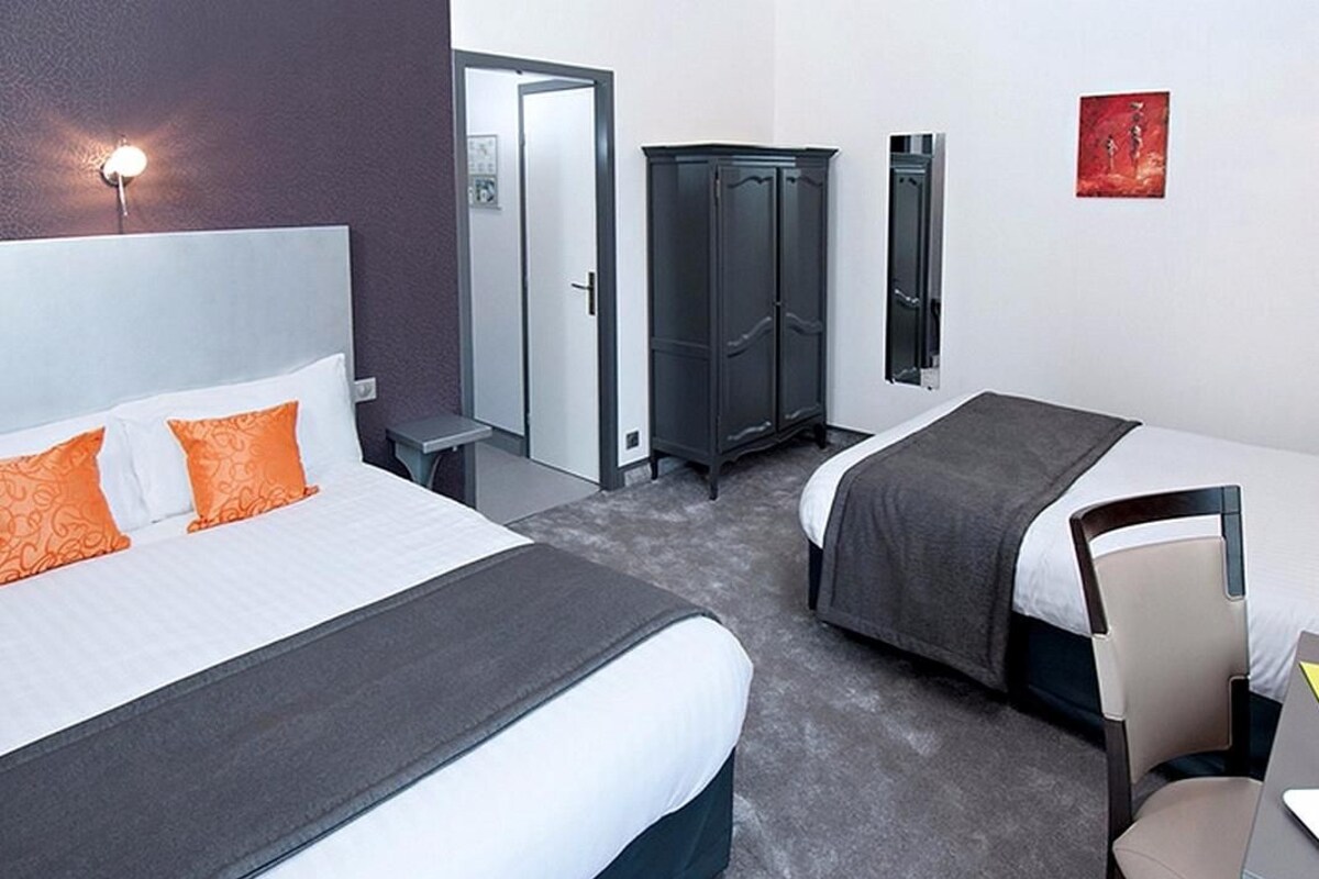 A hotel room with two beds, a wardrobe, a desk, and a chair.