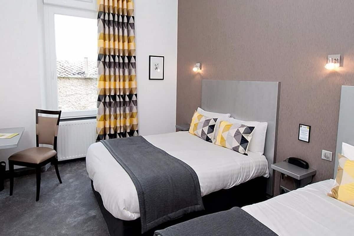 A hotel room with two beds, a desk, a chair, a nightstand, and a window with curtains.
