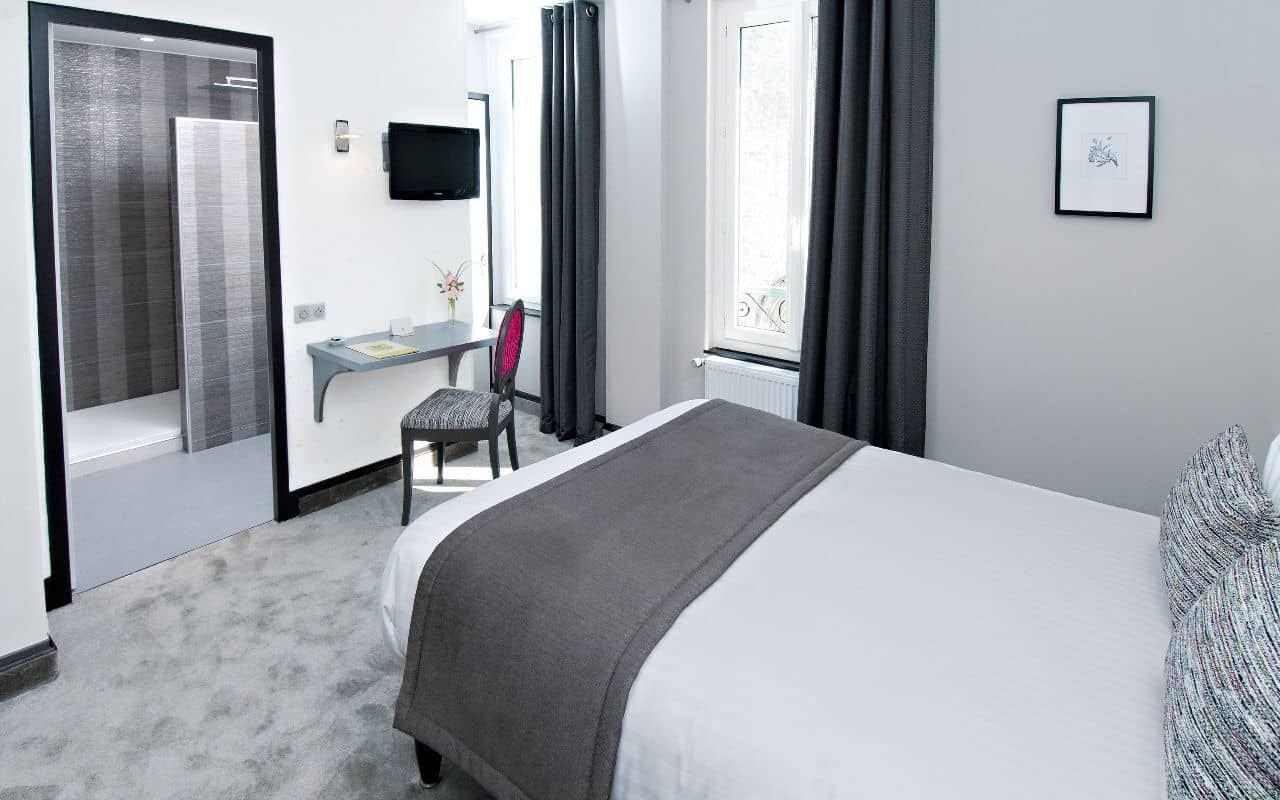 A hotel room with a bed, a desk, a chair, a TV, and a window with curtains.