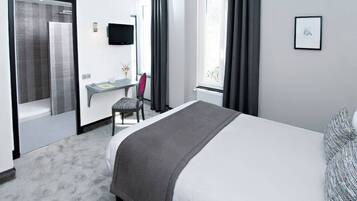 A hotel room with a bed, a desk, a chair, a TV, and a window with curtains.