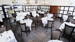 A restaurant with multiple tables and chairs, white tablecloths, and a tiled floor. - Hôtel Nougier (Fursac)