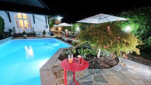 A swimming pool with a red table and chairs, surrounded by stone tiles and greenery. - Hôtel Nougier (Fursac)