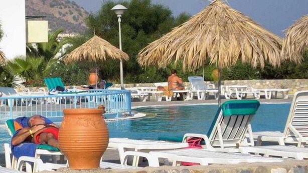 A pool area with lounge chairs and thatched umbrellas, surrounded by a stone wall. - Evripides Village (Kos)