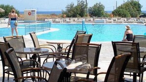 A poolside area with lounge chairs and tables, a lifeguard stand, and a view of the ocean. - Evripides Village (Kos)