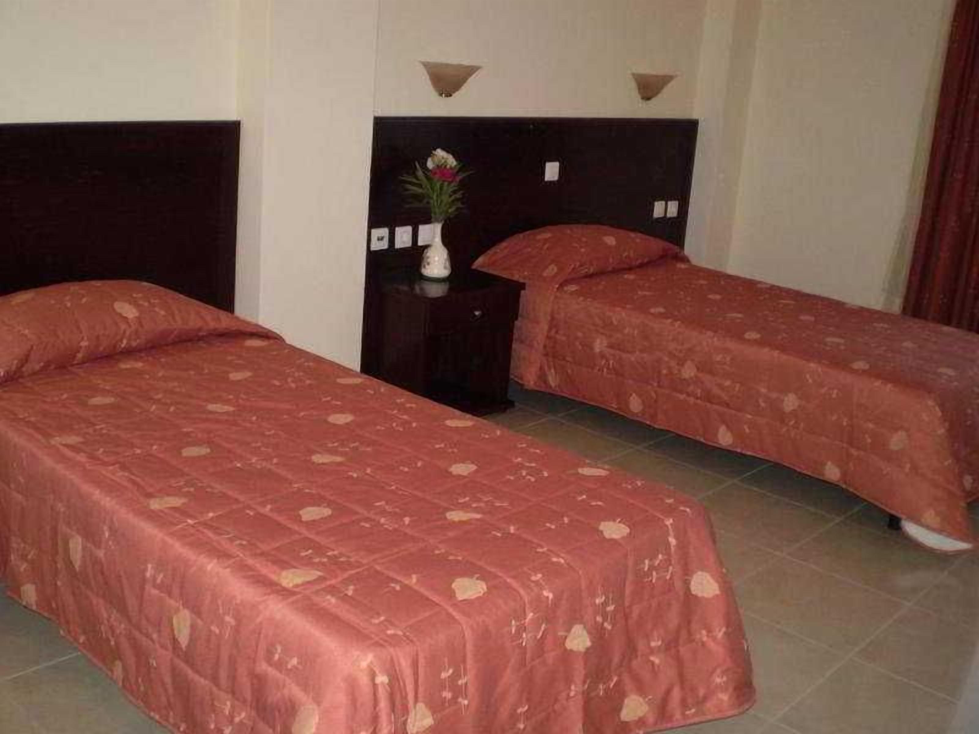 Habitación de hotel con dos camas individuales, una mesita de noche con un jarrón y una lámpara de pared.