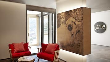 Ein modernes Interieur mit zwei roten Sesseln, einem runden Holztisch und einem großen, abstrakten Kunstwerk an der Wand.