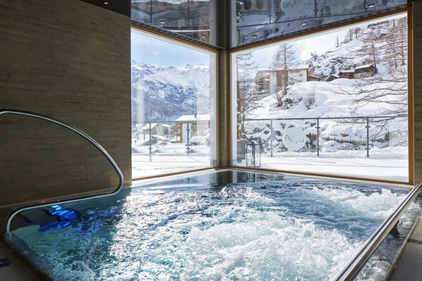Un jacuzzi con vista a montañas nevadas y edificios.