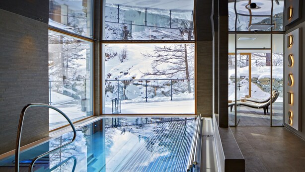 A modern indoor pool area with large windows offering a view of a snowy landscape.