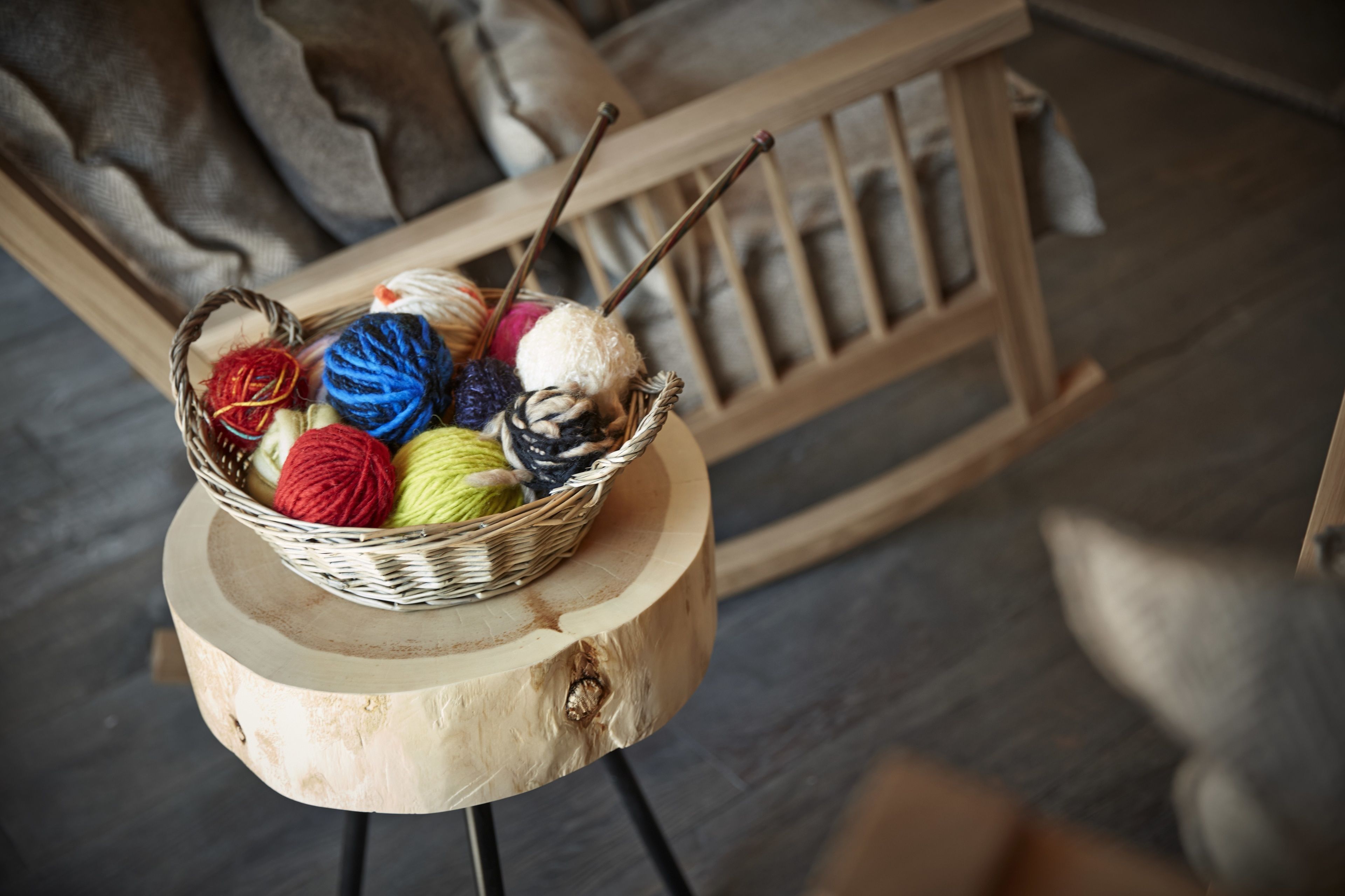 A basket of colorful yarn balls on a wooden stool.
