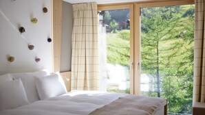 A bedroom with a large bed, a view of greenery through a sliding door, and a wall with decorative elements.