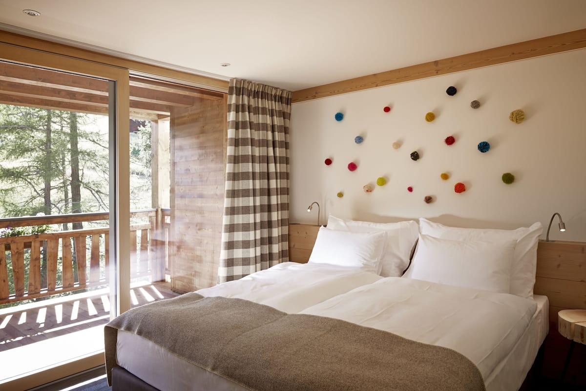 Un dormitorio con una cama grande, un cabecero de madera, una ventana con vistas a árboles y una pared decorada con pompones de colores.