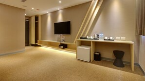 Habitación de hotel con televisor de pantalla plana, un refrigerador pequeño, escritorio con cafetera y un cesto de basura.