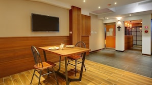 Un comedor con una mesa y sillas de madera, un televisor de pantalla plana en la pared y una cruz decorando la pared.