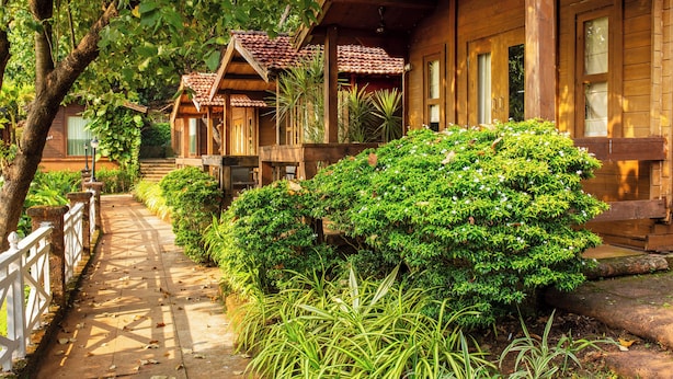 Une cabane en bois avec un toit en tuiles, une véranda et un chemin bordé de verdure.