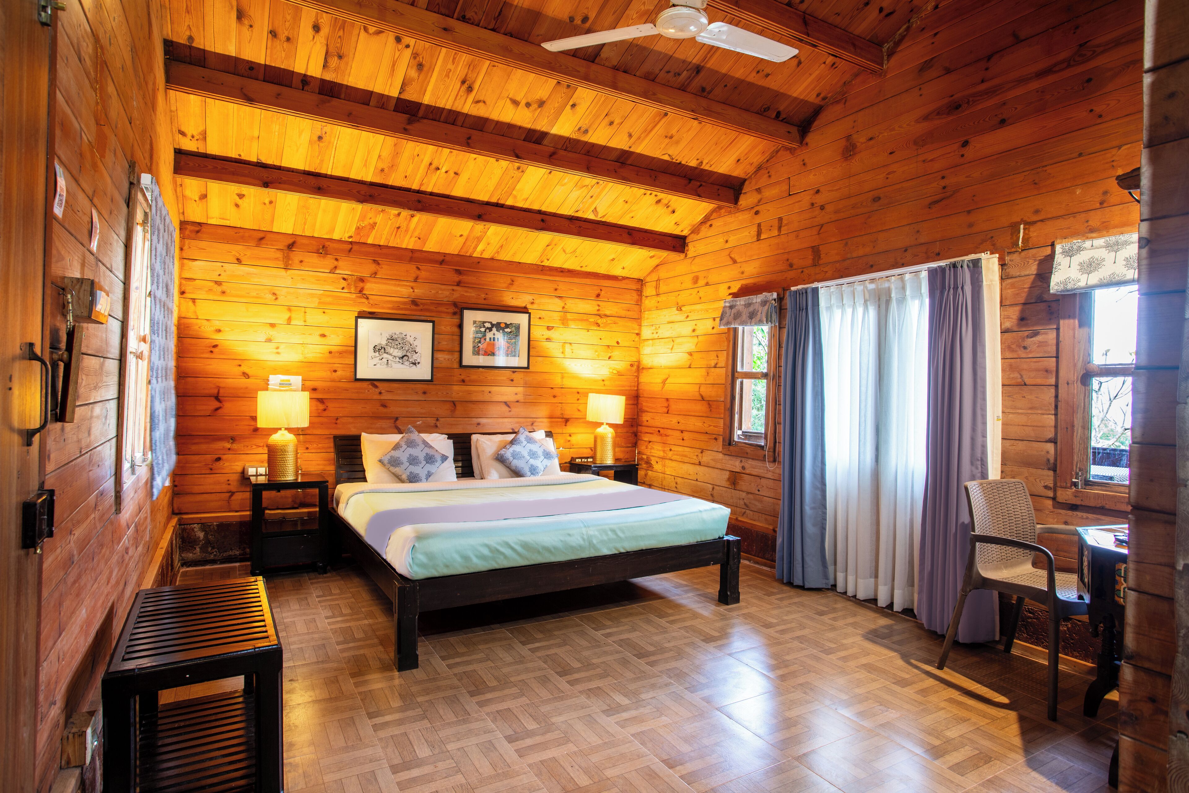 A wooden cabin room with a bed, two bedside tables, a chair, and a ceiling fan.