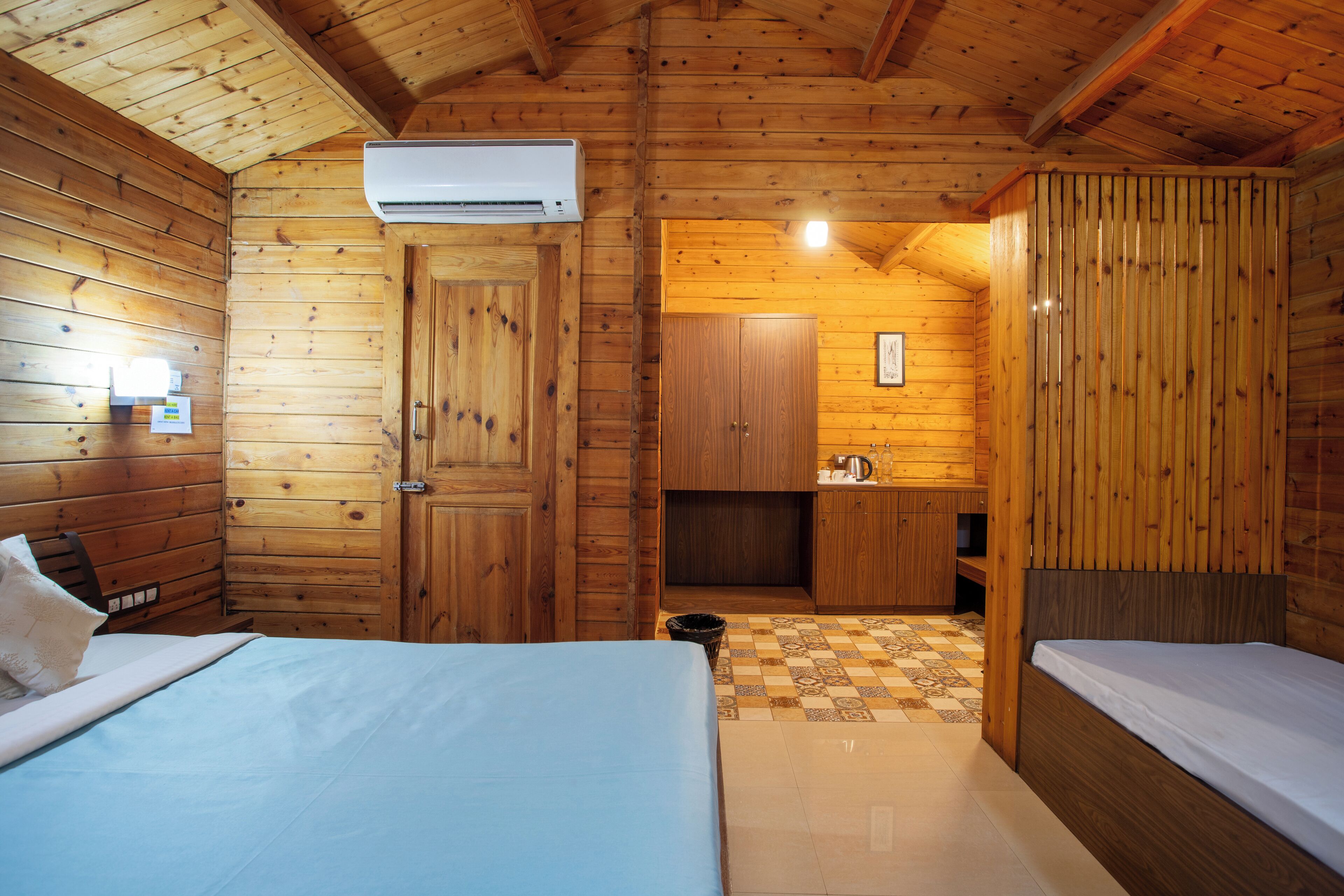 Quarto de cabana de madeira com duas camas, um espaço de cozinha compacto e um ar condicionado.
