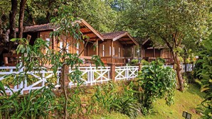 Une cabane en bois avec une clôture blanche, entourée d’une végétation luxuriante.