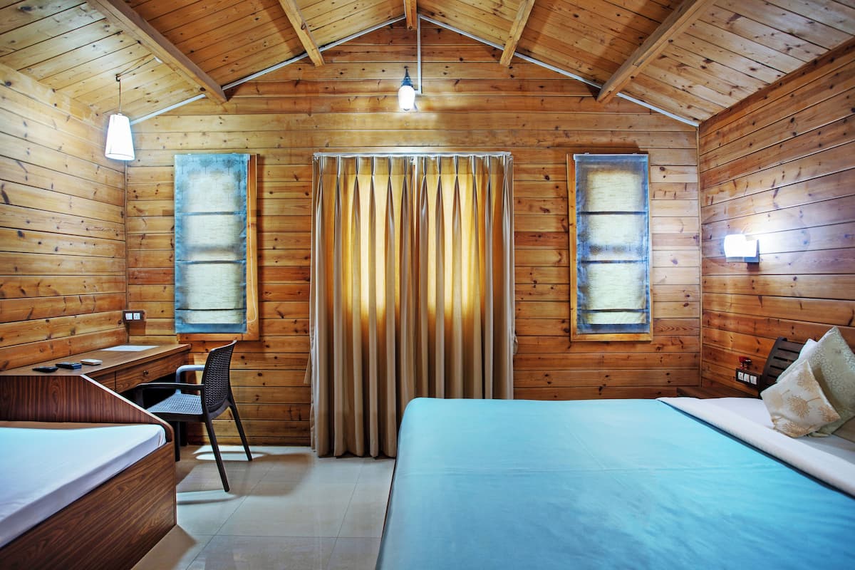 Une chambre dans un chalet en bois, comprenant un lit, un bureau, une chaise et deux fenêtres avec des rideaux.