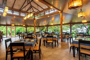 Un espace de restauration intérieur avec des tables et des chaises, de grandes fenêtres et des luminaires suspendus.