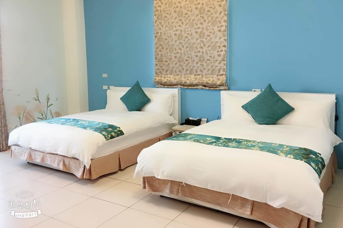 Two twin beds with white and teal bedding, a patterned curtain, and a tiled floor.