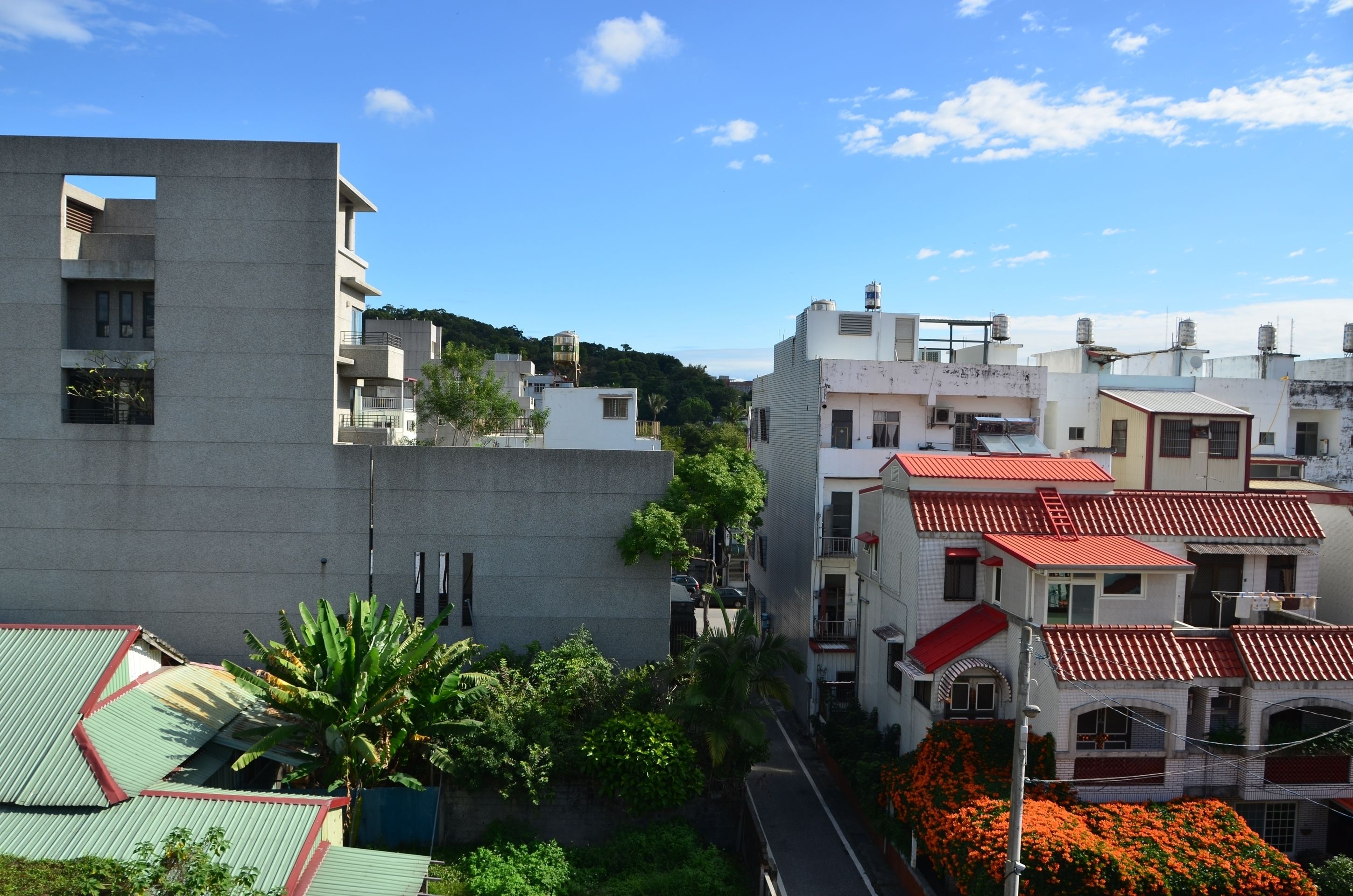 A residential area with modern buildings, a narrow street, and a hill in the background.
