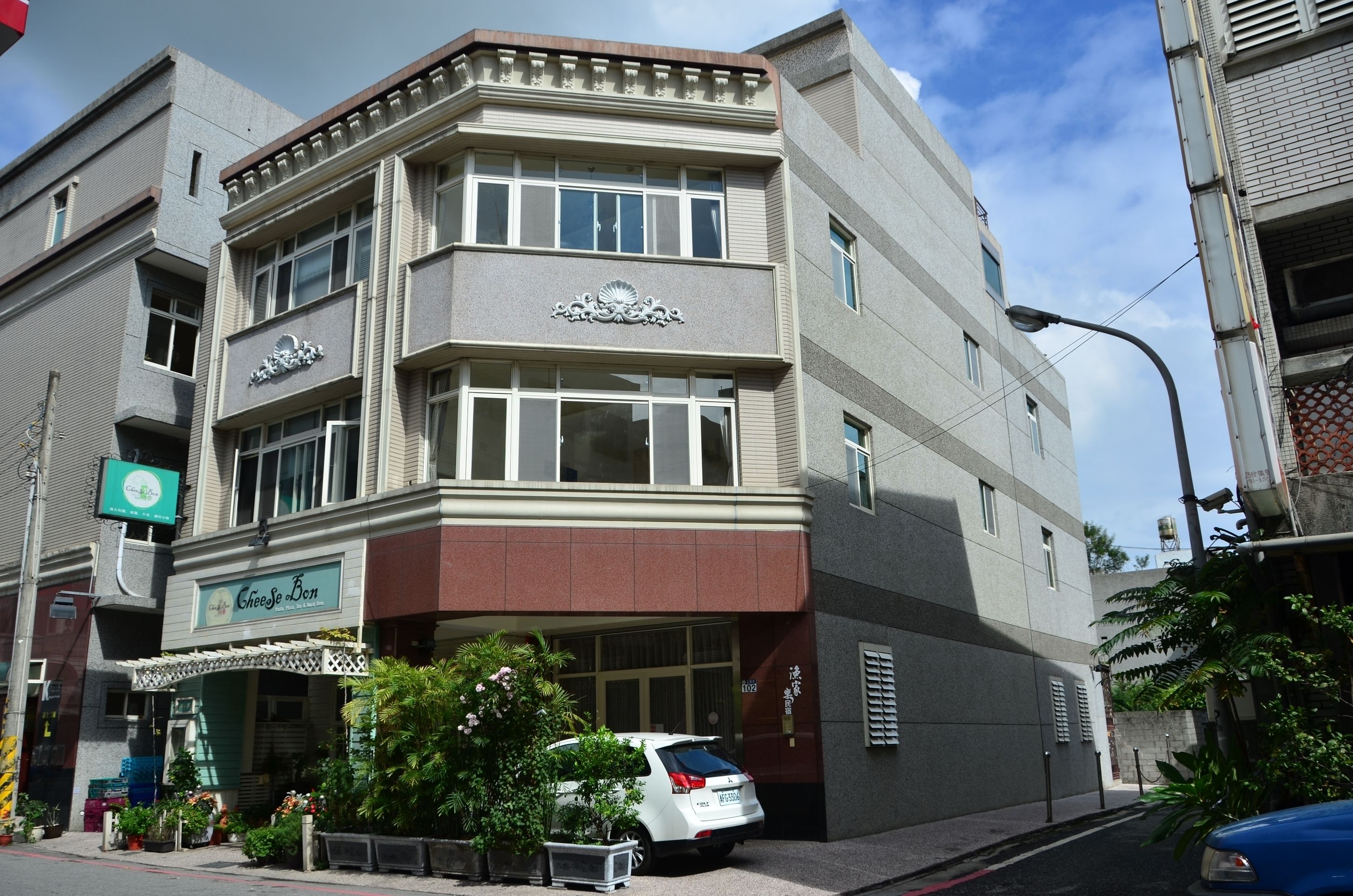 A corner building with a Cheese Bin sign, a white car parked in front, and a street lamp.