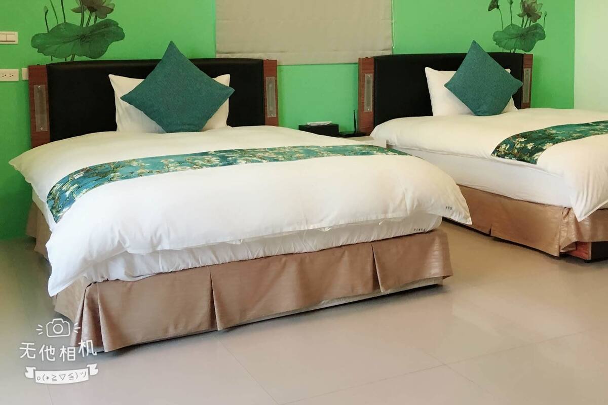 A hotel room with two beds, green walls, and floral wall art.