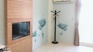 A room with a wooden accent wall, a mounted TV, a wall-mounted air conditioner, a coat rack, and a window with curtains. - Fishfun House (Hualien City)