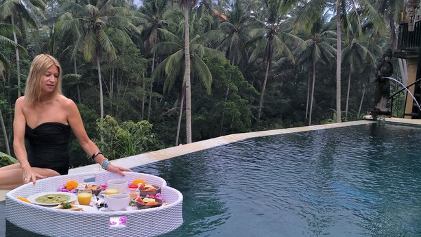 A person sitting by a pool with a table of food and drinks. - Capung Sakti Villas – By Fair Future Foundation (Ubud)