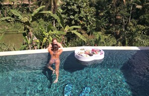 Uma pessoa relaxando em uma piscina transparente com uma cesta de vime contendo comida e bebidas.
