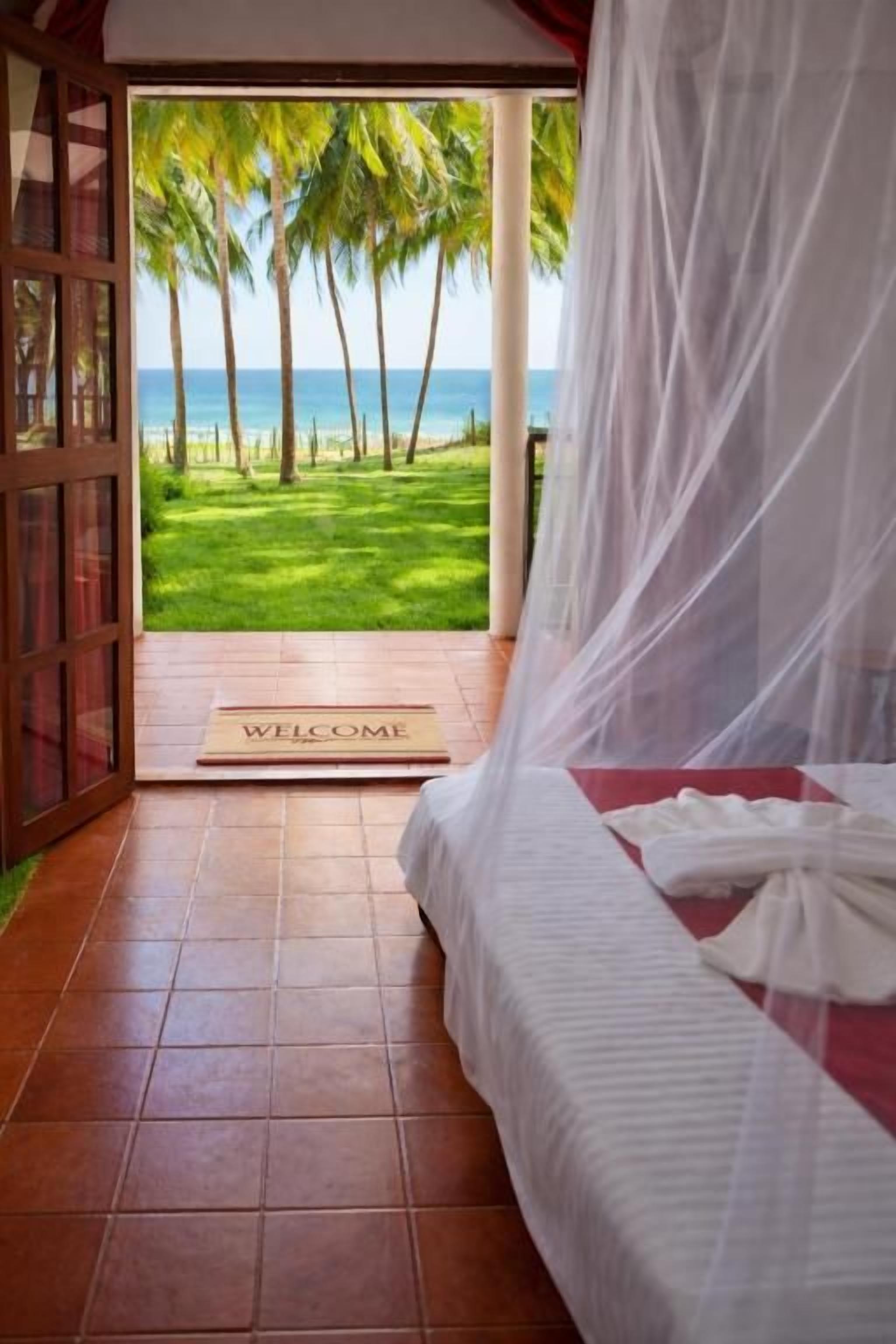 A bedroom with a bed, a white canopy, and a view of a beach with palm trees.
