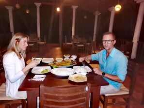 A dining table with plates of food, a man and a woman sitting across from each other. - Helios Beach Resort (Rekawa)