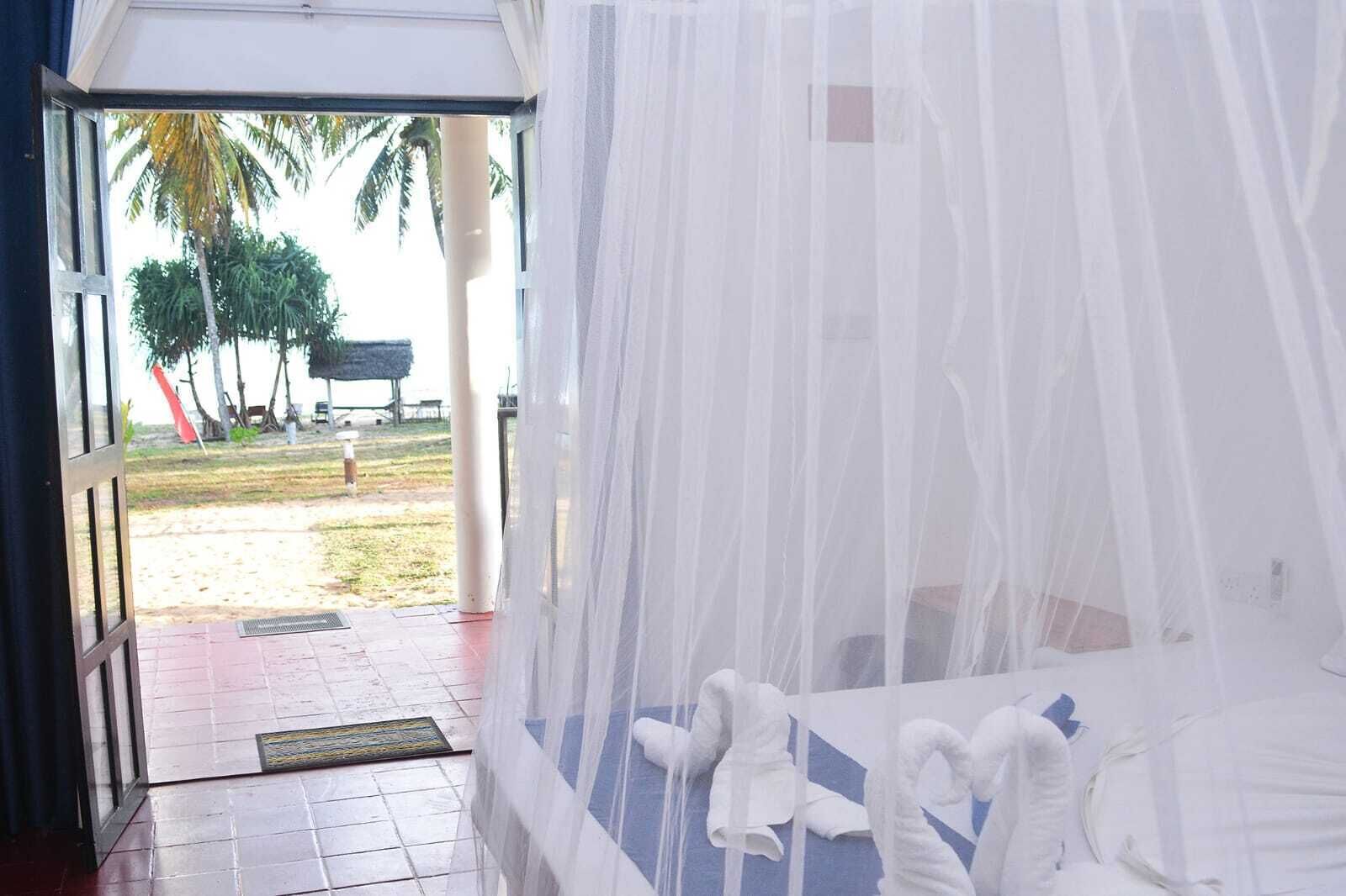 A room with a bed covered by a white canopy, a view of palm trees outside, and a tiled floor.