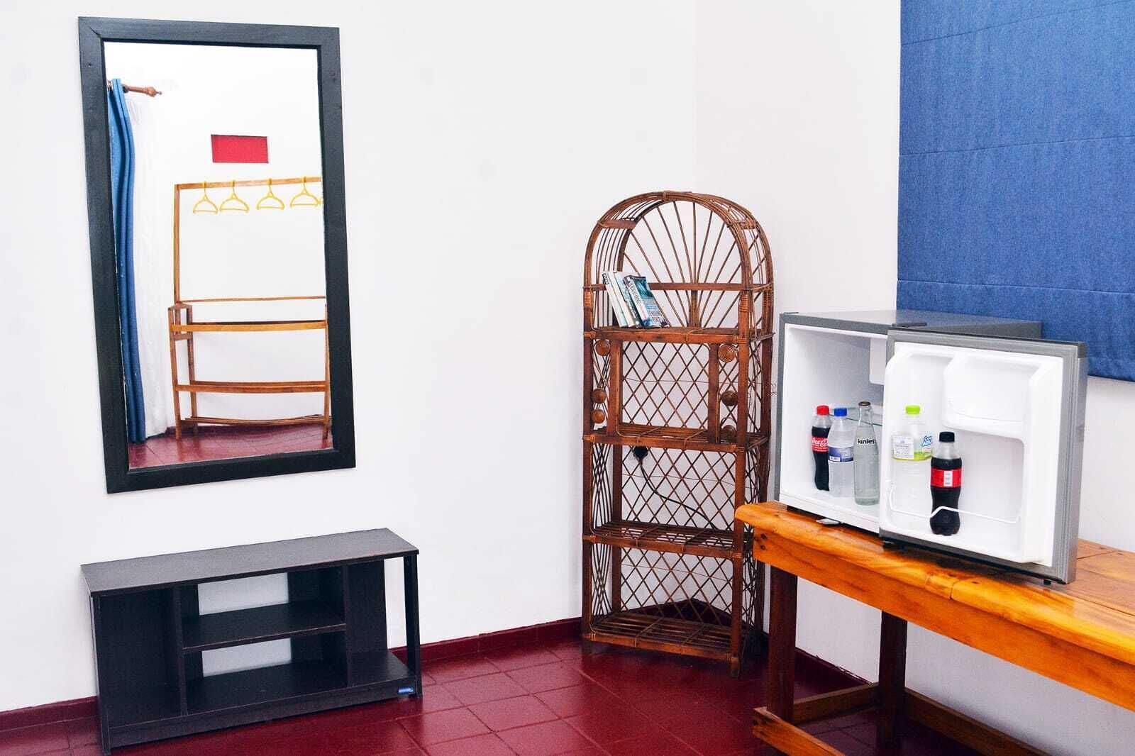 A room with a mirror, a wooden chair, a small table with a television, and a shelf with beverages.