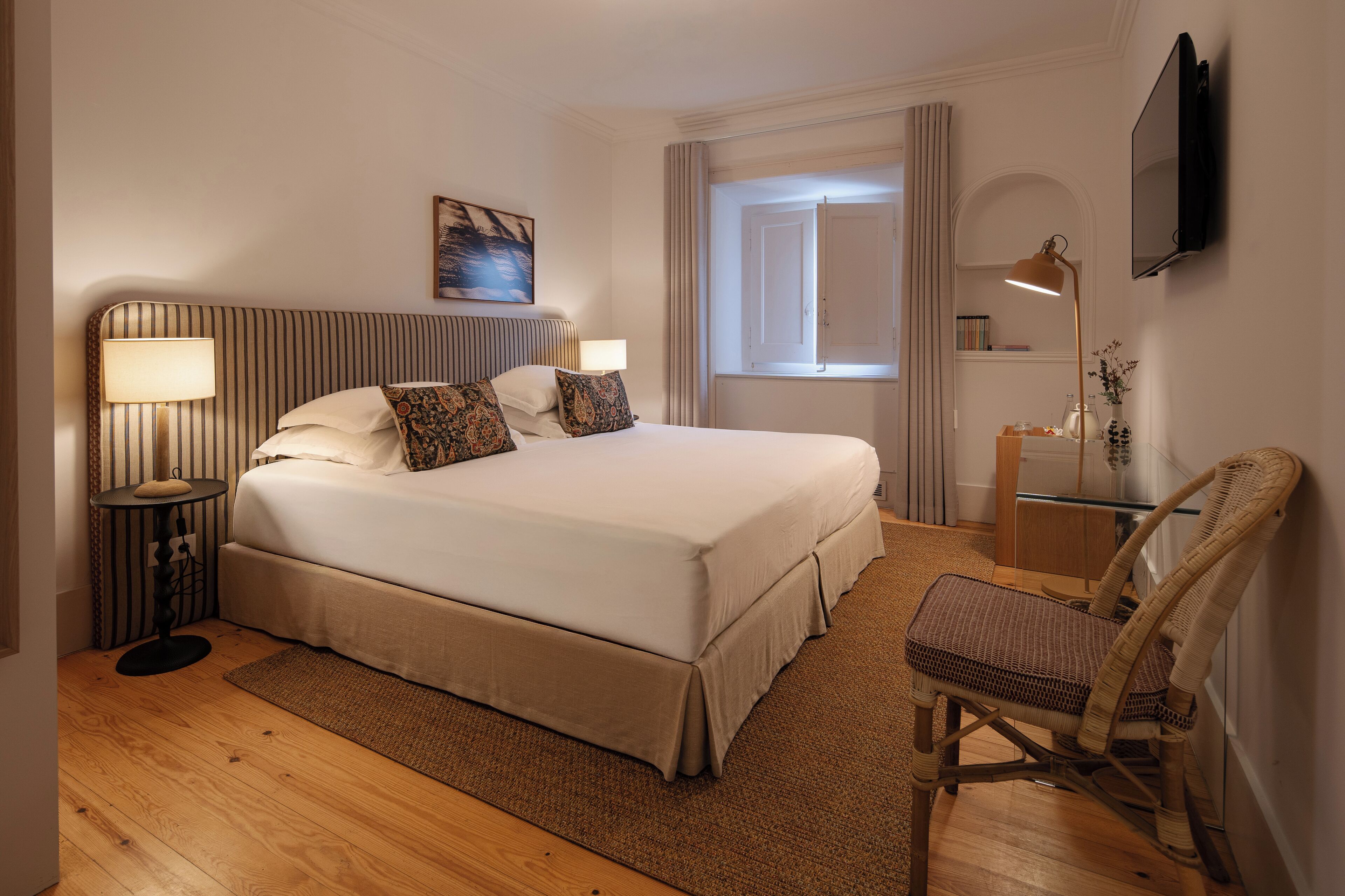 Ein Hotelzimmer mit einem großen Bett, Nachttischlampen, einem Sessel, einem Fernseher und einem Fenster mit Vorhängen.