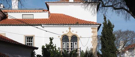 Un edificio con techo de tejas rojas, una ventana arqueada central y fachada blanca.
