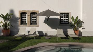 Una piscina con reflejos, un edificio blanco con ventanas y sillones de descanso.