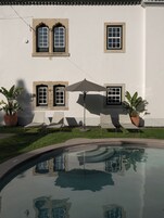 Una piscina con reflejos, un edificio blanco con ventanas y sillones de descanso.