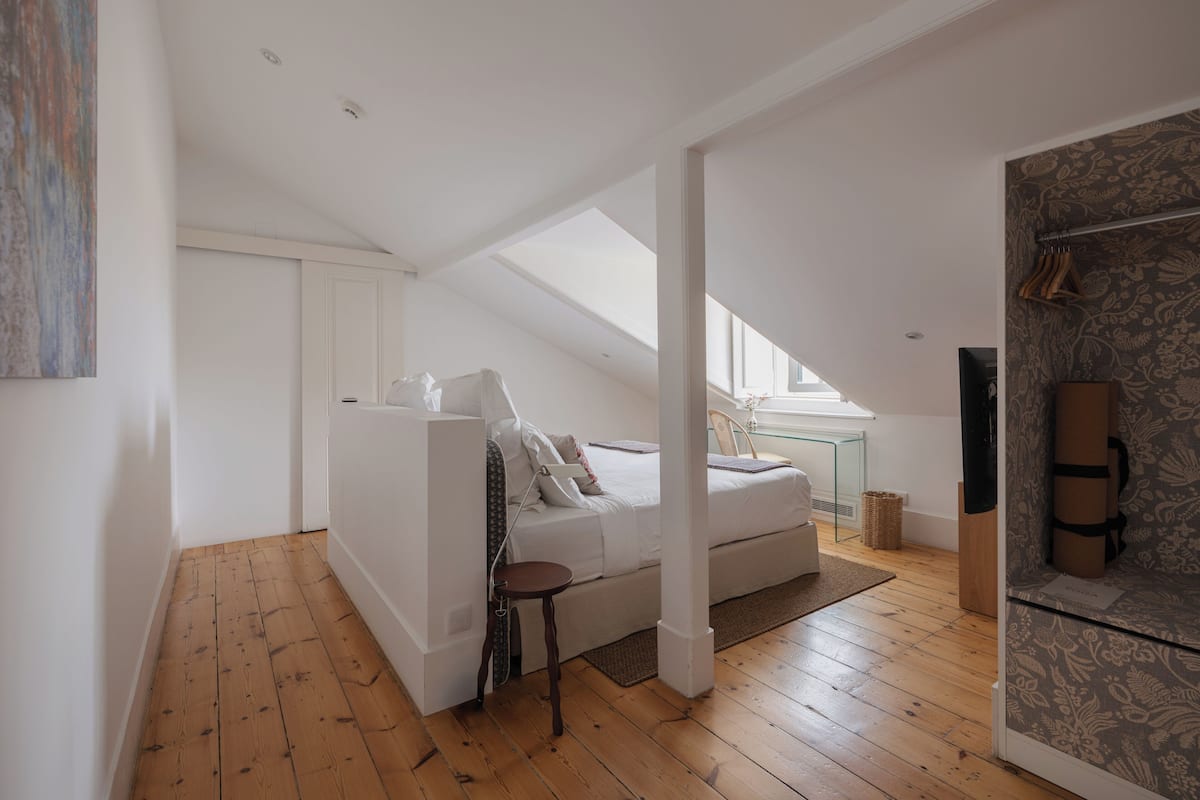 Een moderne loft slaapkamer met een schuine wand, een glazen bureau en een groot raam.