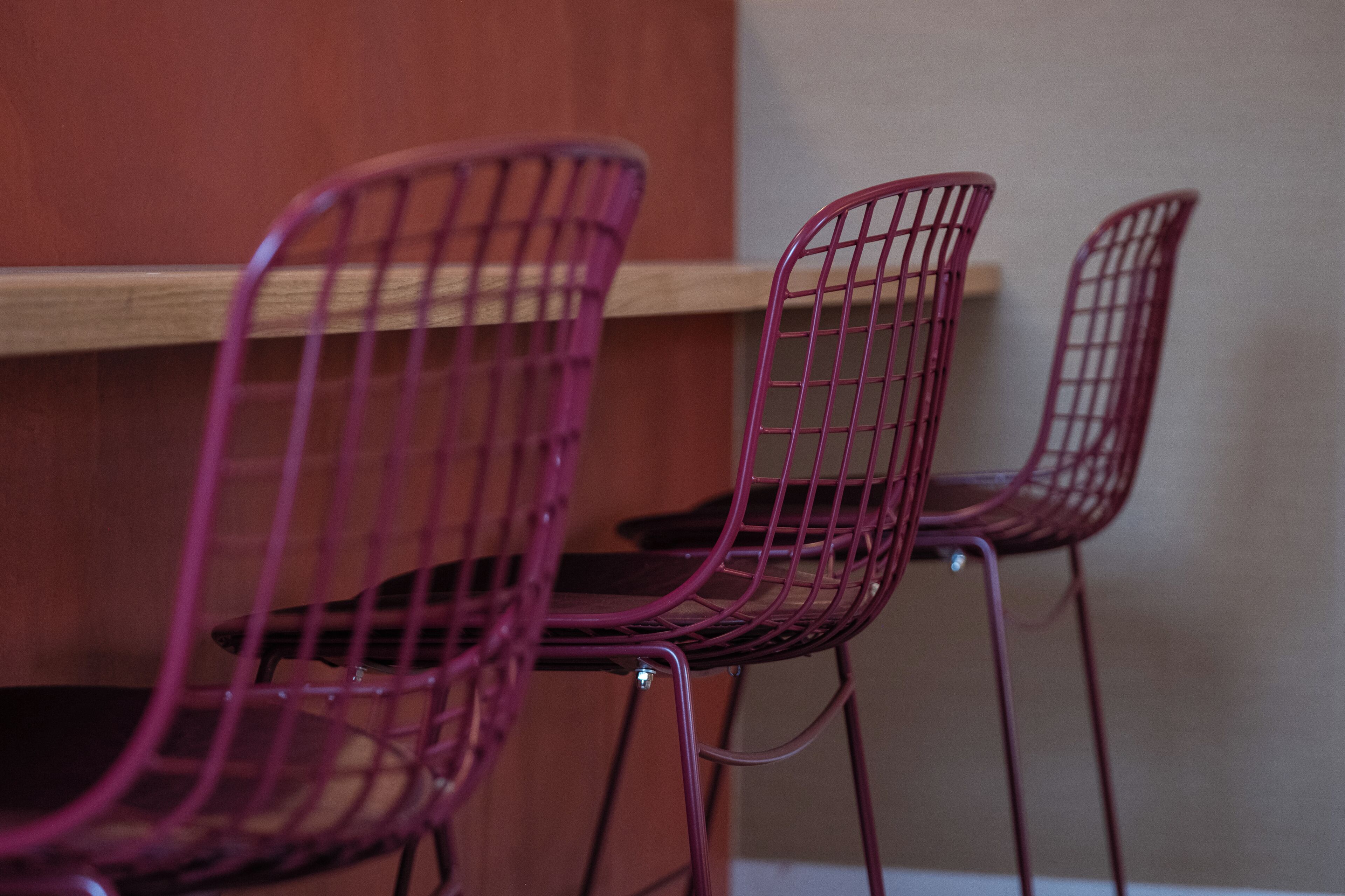 Trois chaises violettes à armature métallique et pieds en métal, placées devant une table en bois et un mur beige.