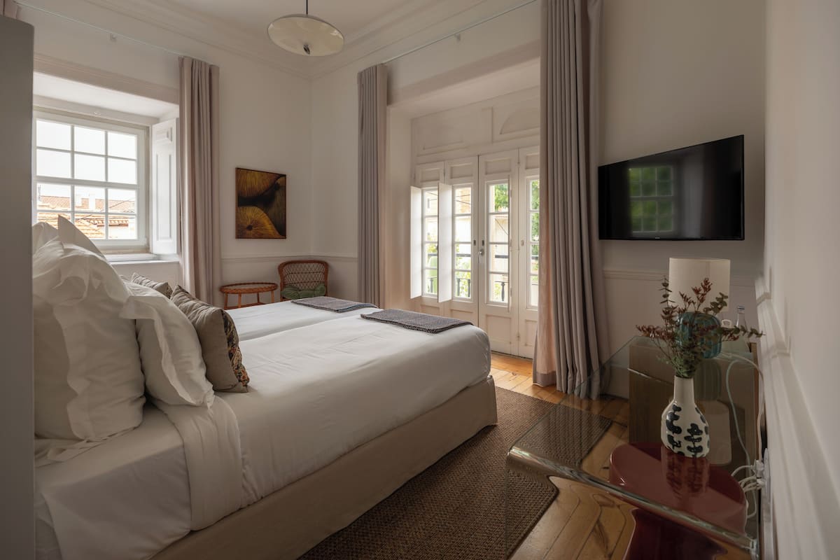 Een hotelkamer met een groot bed, een televisie, een tafeltje met een vaas en een stoel.