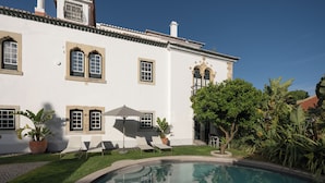 Una piscina con reflejo cristalino, un edificio blanco con amplias ventanas y un césped cuidado.