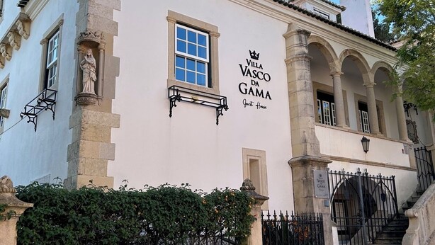 Un edificio con el letrero 'Villa Vasco da Gama Guest House'. Presenta un estilo arquitectónico clásico con columnas y arcos.