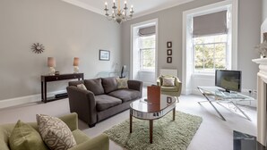 A living room with a sofa, armchairs, a glass coffee table, a TV, and a fireplace. - Destiny Scotland - Q-Residence (Edinburgh)